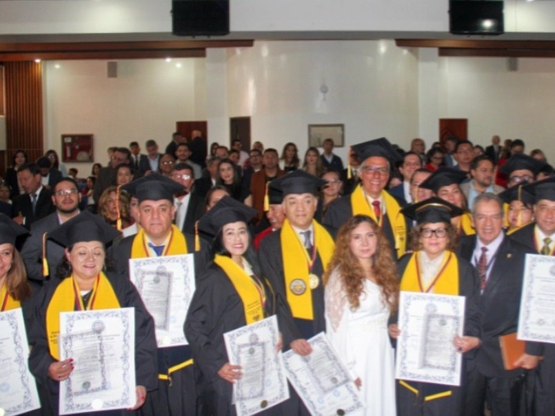 Graduados de TIU Miami con toga, banda dorada y diplomas en un auditorio lleno