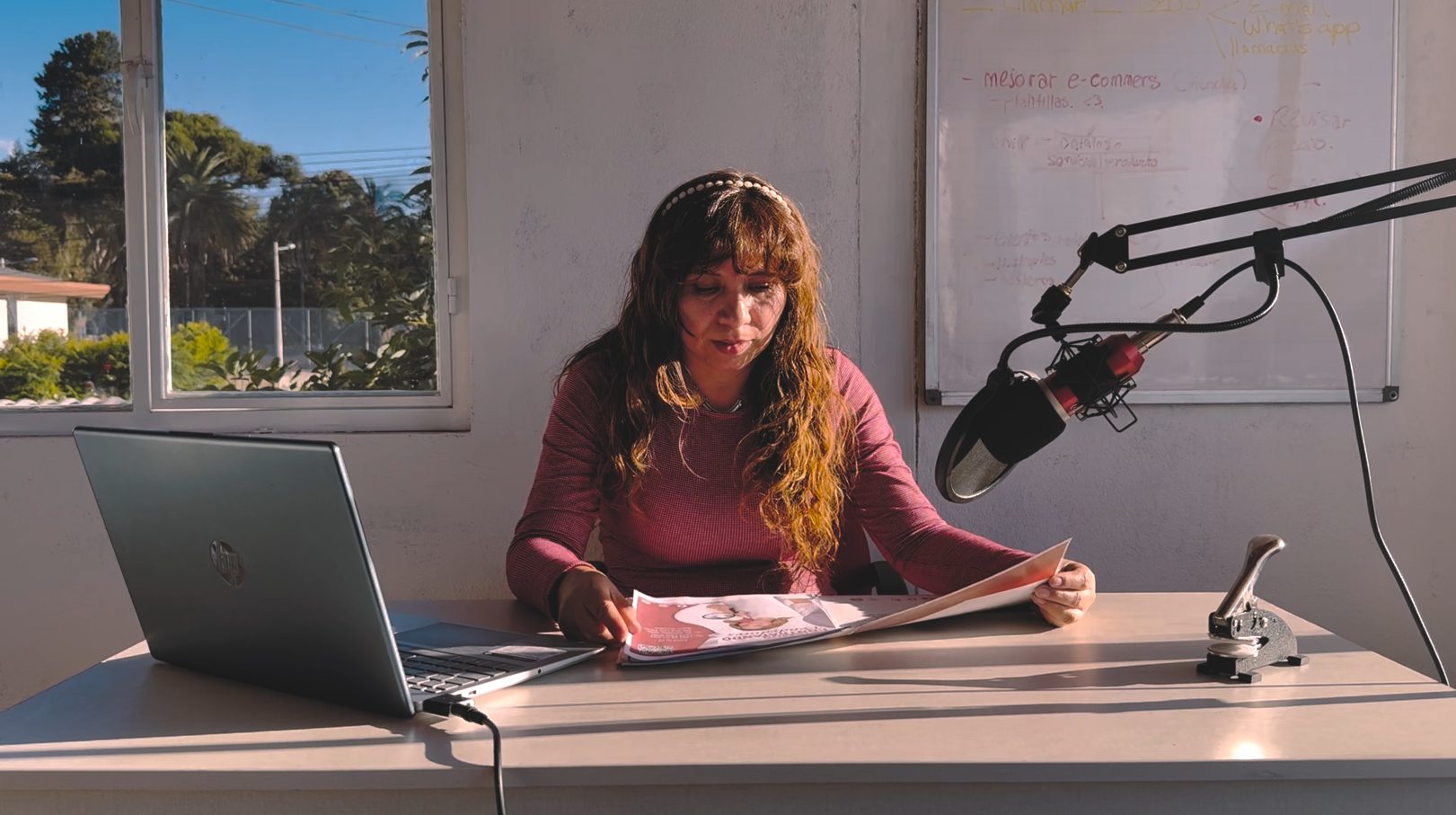 Mujer trabajando en un escritorio con su laptop, un micrófono y un periódico abierto